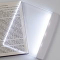 Fixless LED flat panel reading light laid over an open book page with edge-lit glow